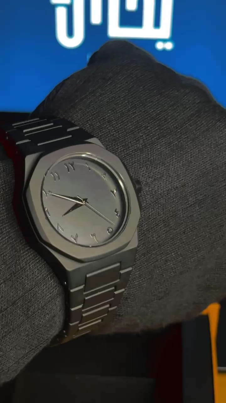 Black wristwatch on a person's wrist with a blue background