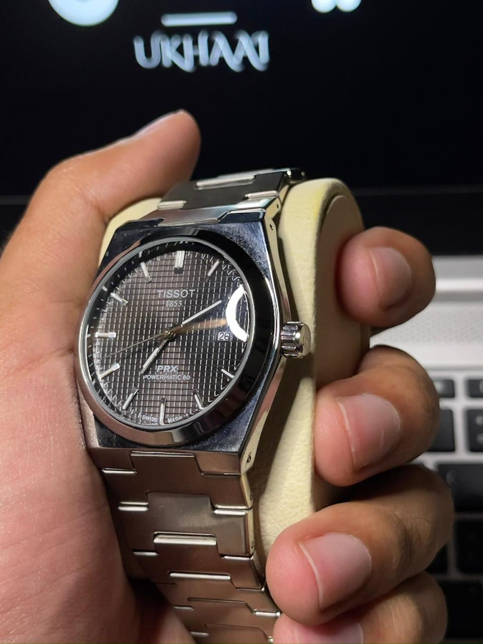 Hand holding a silver Tissot watch with a blurred background